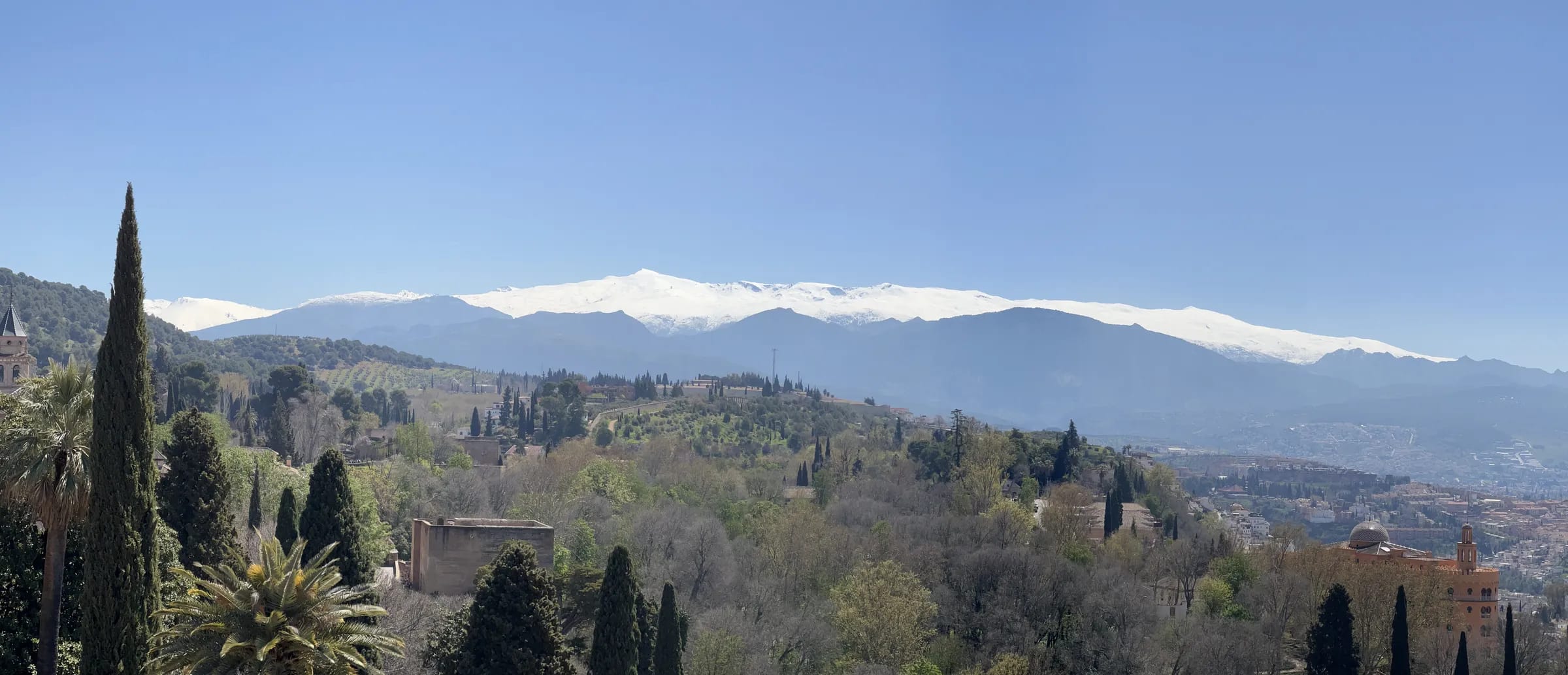 Panorama of a hillside town below snow-capped mountains